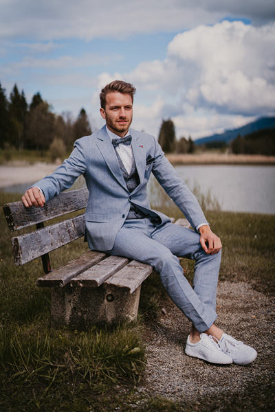 Der Bräutigam sitzt wartend auf der Bank und er trägt einen blauen Hochzeitsanzug